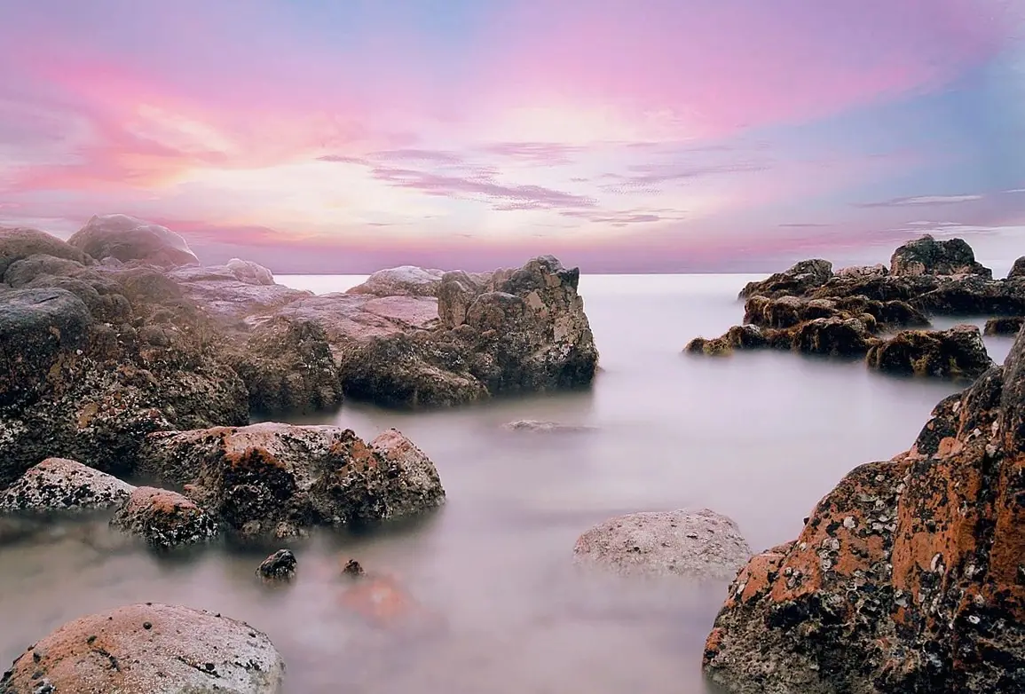 夕焼け空の下、穏やかな海に岩が連なる磯の風景